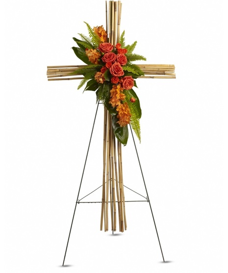 A funeral spray with roses and greenery in front of a wood assembled cross