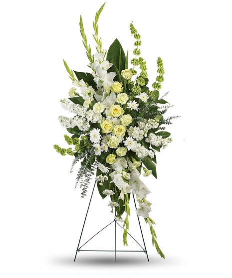 A tall, elegant floral arrangement with white roses, gladiolus, chrysanthemums, and lush greenery on a black metal stand.