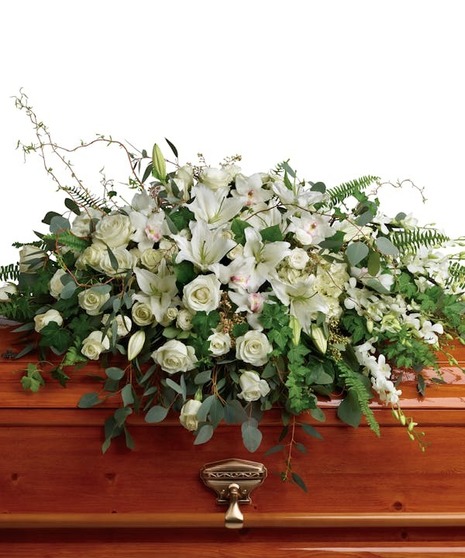 White flowers and green leaves over a brown casket.