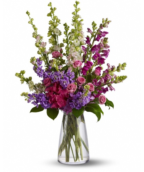 arrangement of larkspur, snapdragons and spray roses that are gathered gracefully in a glass vase.